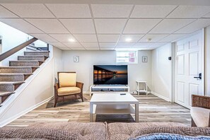 A living room with a TV, a sofa, a chair, a coffee table, and a staircase. - Now avail Beach Block Getaway (Atlantic City)