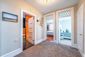 A hallway with a carpeted floor, a door leading to a bathroom, and a bedroom visible through an open door.