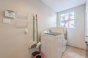 A laundry room with a washing machine, a dryer, a window with flowers, and a wall-mounted control panel. - Now avail Beach Block Getaway (Atlantic City)