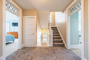 A hallway with a carpeted floor, a white door, a staircase with a patterned carpet, and a glass door with a decorative frame. - Now avail Beach Block Getaway (Atlantic City)