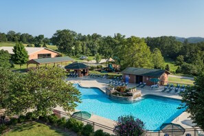 A swimming pool with lounge chairs and a gazebo, surrounded by greenery and a building with a sloped roof.