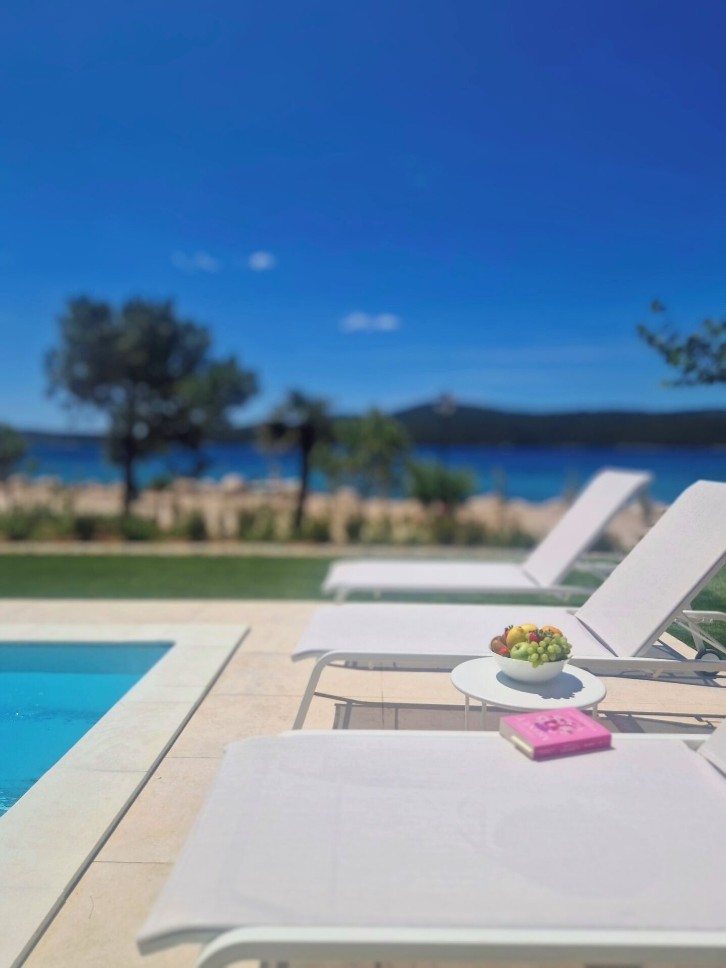 Un espace aménagé au bord de la piscine, avec des chaises longues et une table sur laquelle on trouve des fruits et un objet rose.