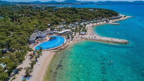 An aerial view of a coastal resort with a large swimming pool, beach, and clear turquoise waters. - Amadria Exclusive Beach Villa (Sibenik)