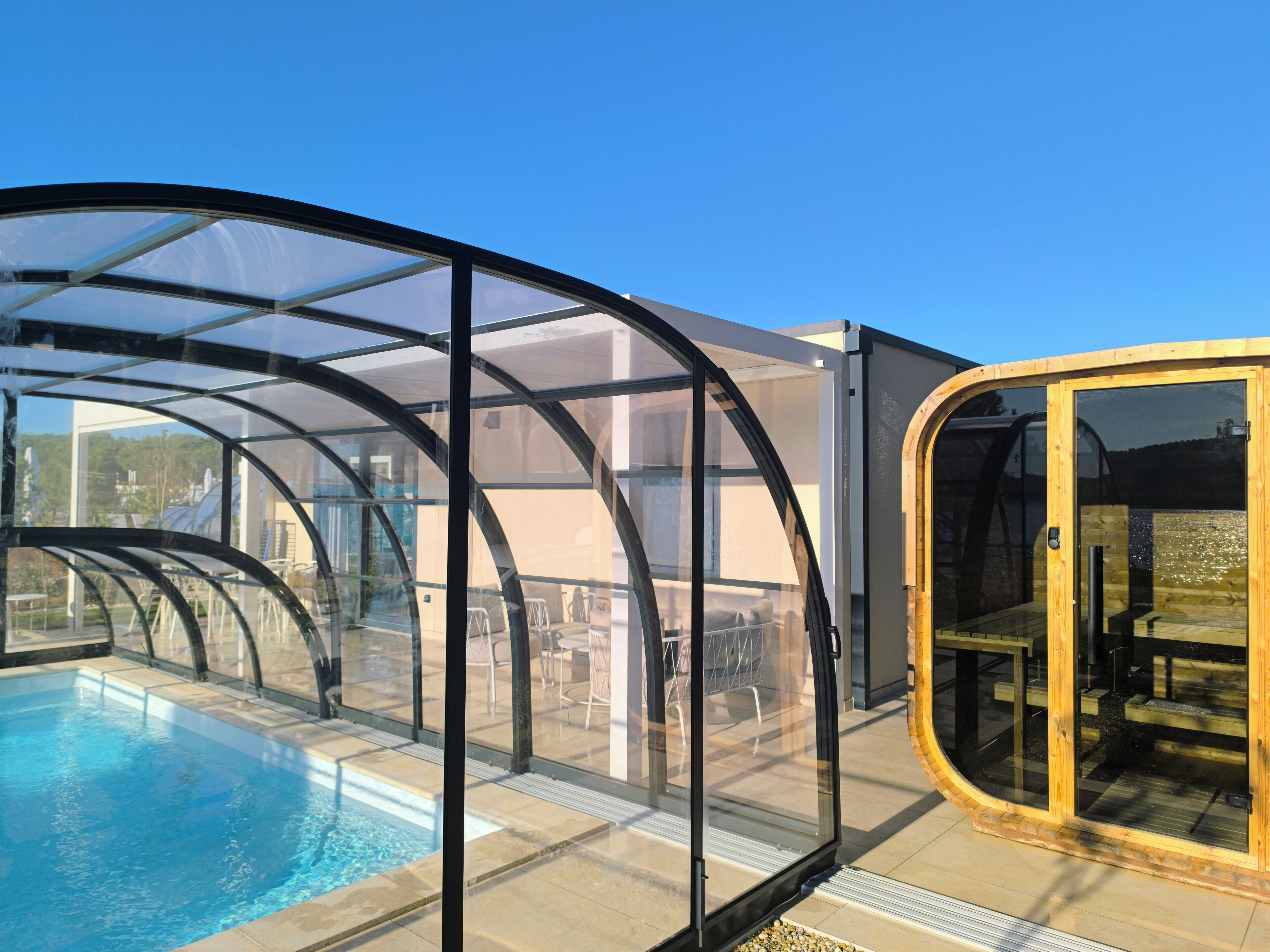 A glass-enclosed swimming pool with a wooden deck and a covered seating area.