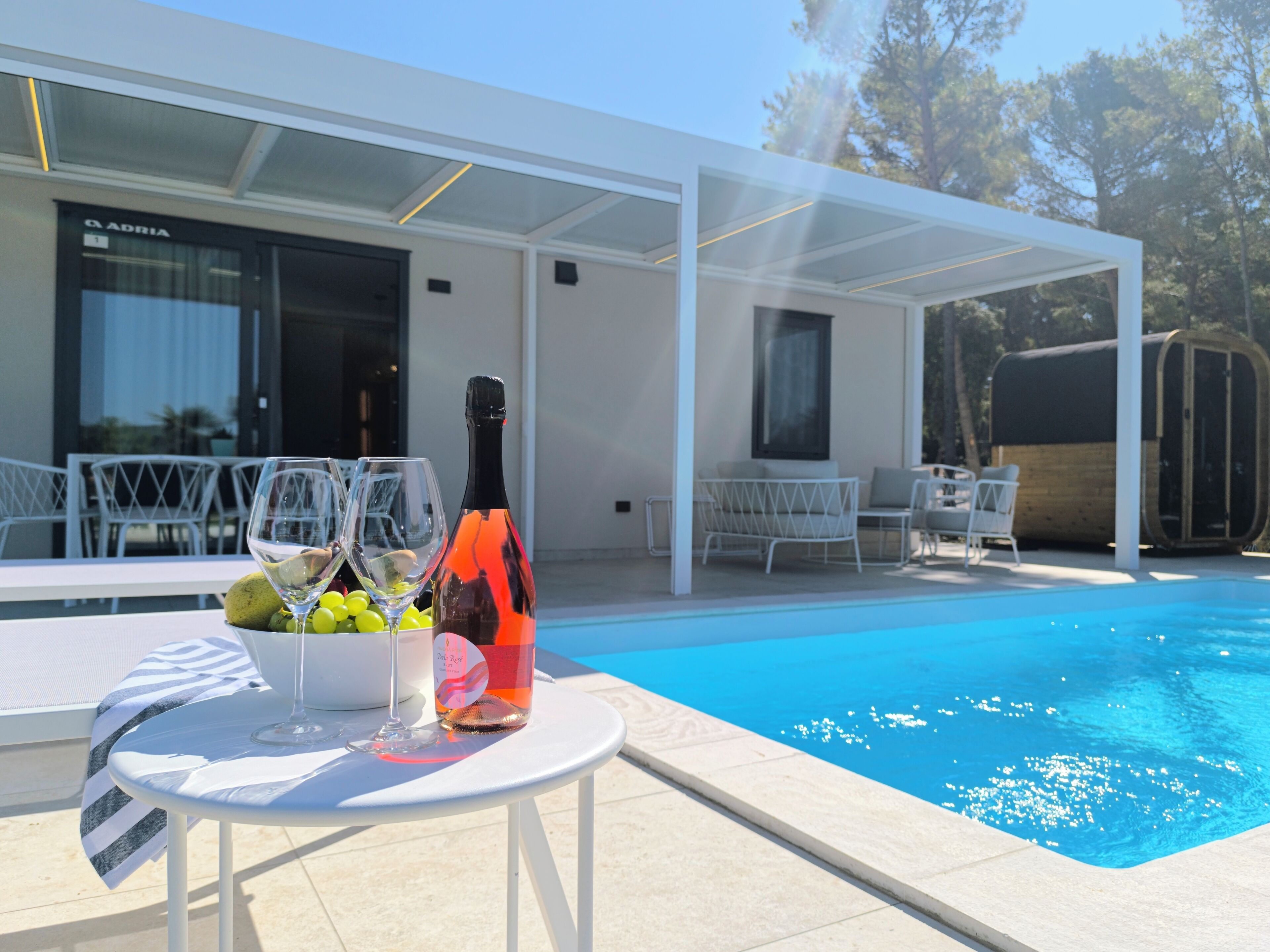 Un espace aménagé au bord de la piscine, avec une table, une bouteille de vin et un saladier de fruits.