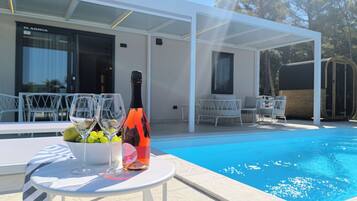 Un espace aménagé au bord de la piscine, avec une table, une bouteille de vin et un saladier de fruits.