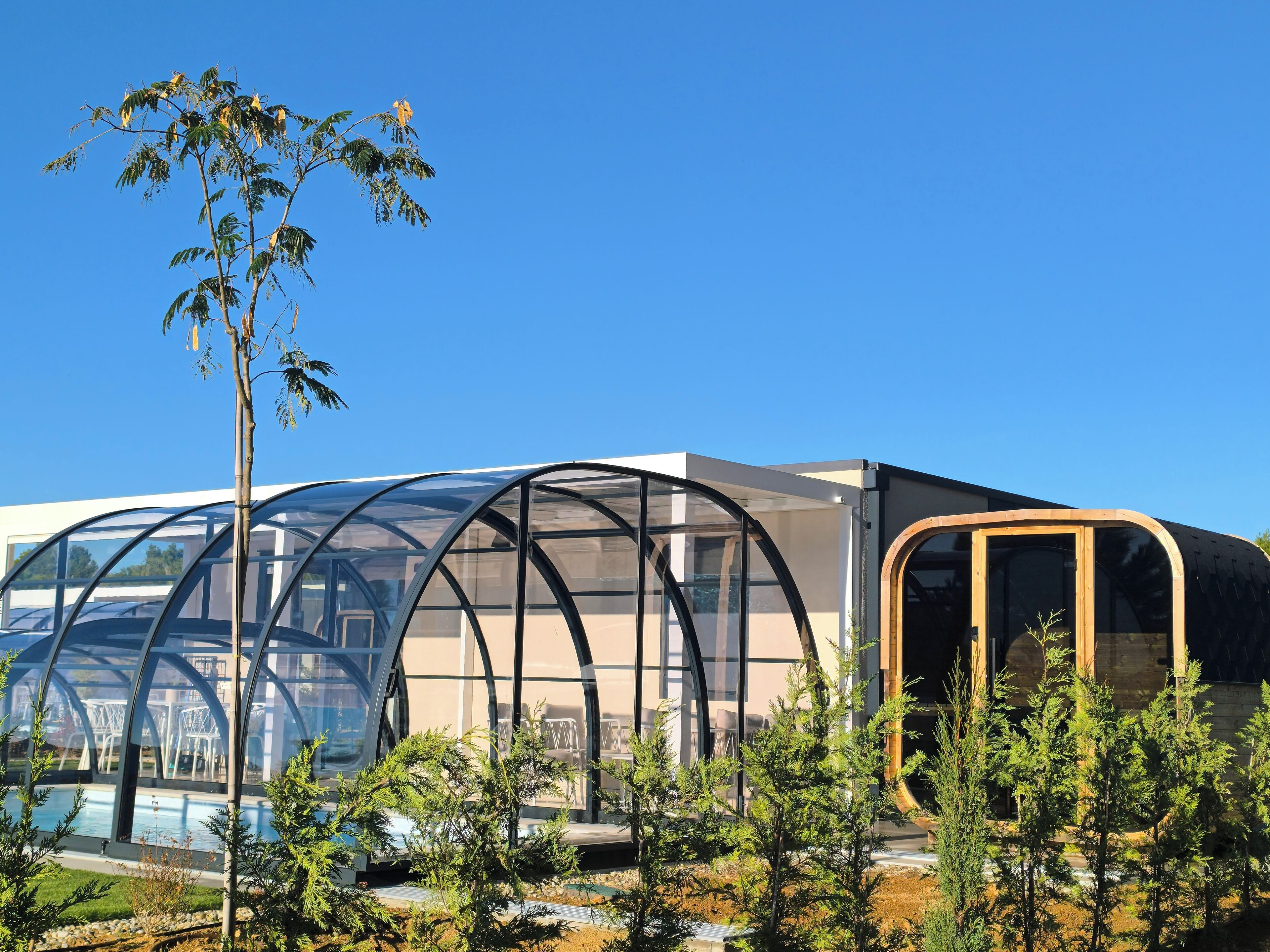 Edifici modern amb una estructura de trencadissa de vidre, envoltat d'arbres i una piscina.