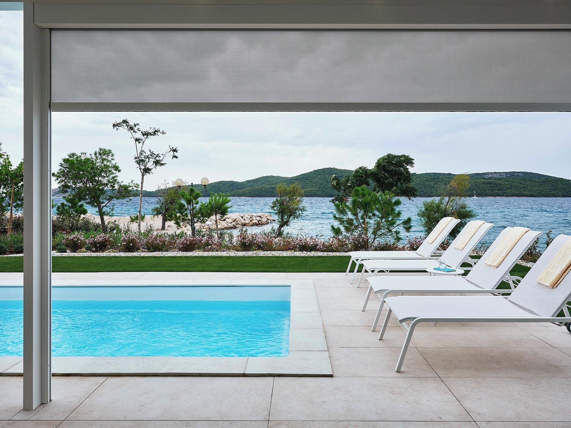 Zona junto a la piscina con sillones de descanso y vistas al mar y las colinas.