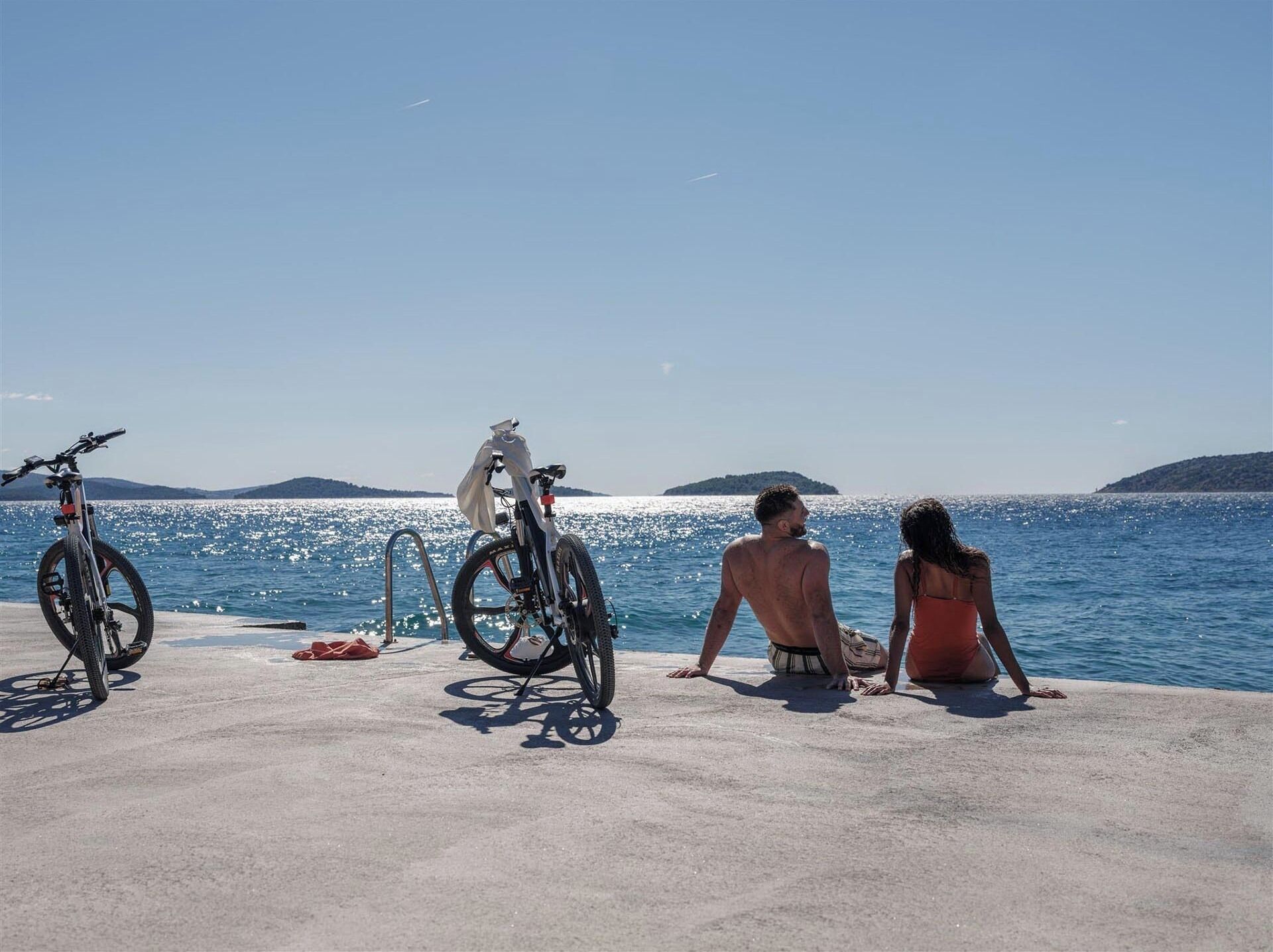 A concrete platform by the sea with two bicycles and two people.