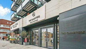 Un edificio moderno con il cartello "The Quarters", caratterizzato da un ingresso in vetro e un fioriere esterna.