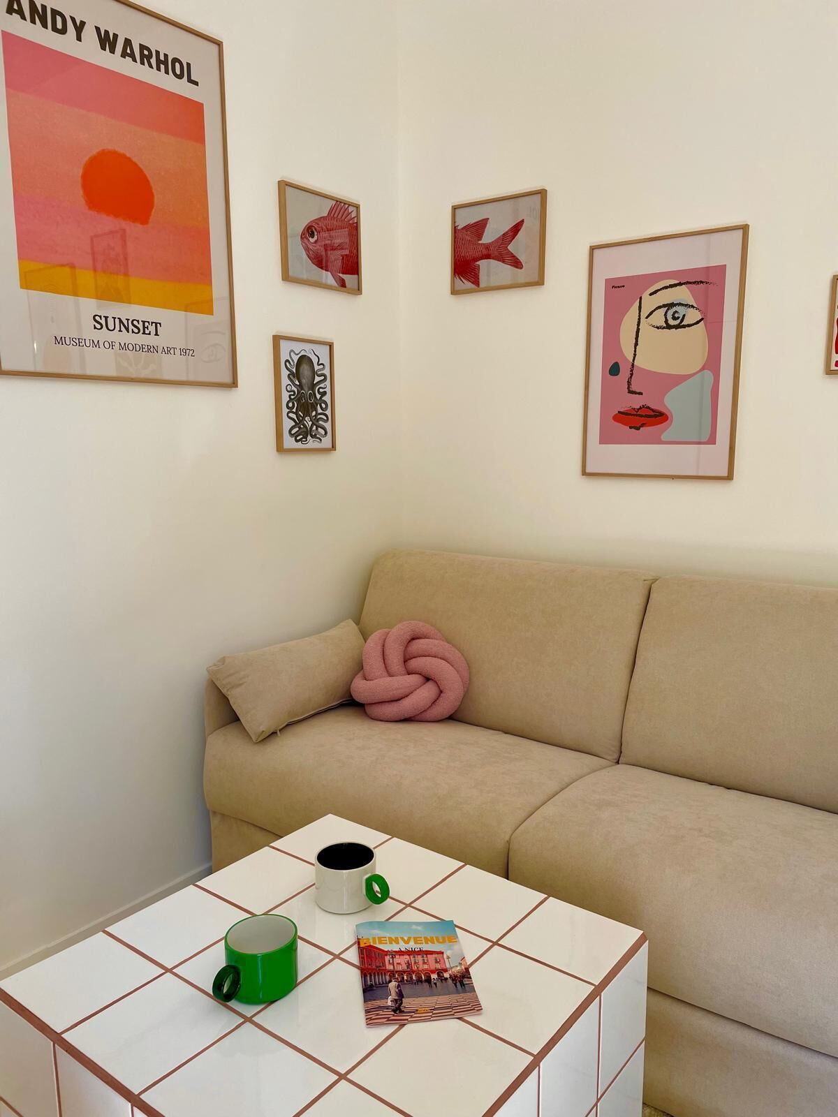 A living room with a beige sofa, a white coffee table with two mugs, and framed artwork on the wall.