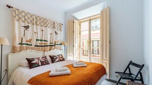 A hotel room with a bed, a chair, a table, and a window with an open door. - Cathedral PentHouse (Sevilla)