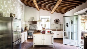 A kitchen with a stainless steel refrigerator, white cabinets, a wooden ceiling, and a large window.