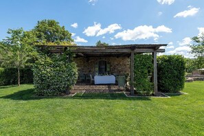 Un edificio de piedra con una pérgola, una mesa y sillas en un jardín.