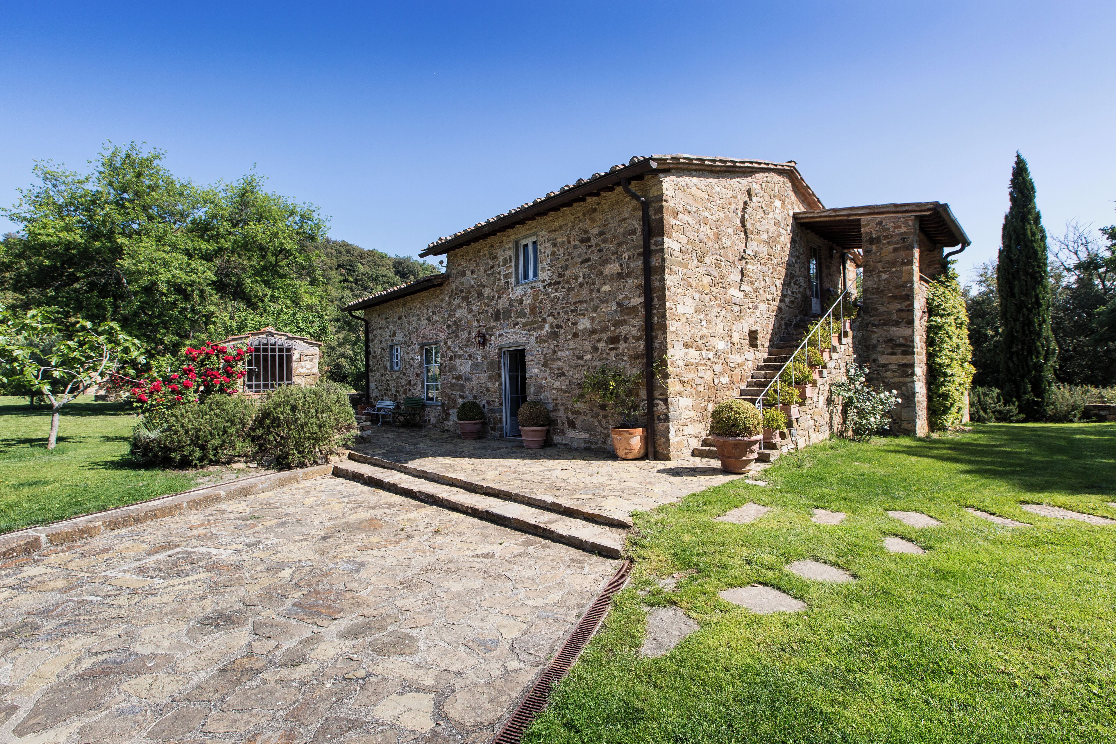 A stone house with a stone pathway leading to the entrance, surrounded by greenery and potted plants.