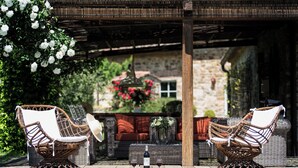A patio with wicker furniture, a table with wine glasses, and a stone building in the background.