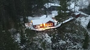 A cabin with a metal roof, surrounded by snow-covered ground and trees. - Holiday home Tived - directly on lake, sauna, boat, hot tub (Tivedstorp)
