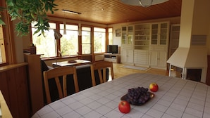 A spacious kitchen with wooden cabinets, a dining table with chairs, and a TV. - Holiday home Tived - directly on lake, sauna, boat, hot tub (Tivedstorp)