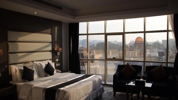 Une chambre d’hôtel avec un grand lit, un bureau, deux chaises et une grande fenêtre donnant sur la ville.