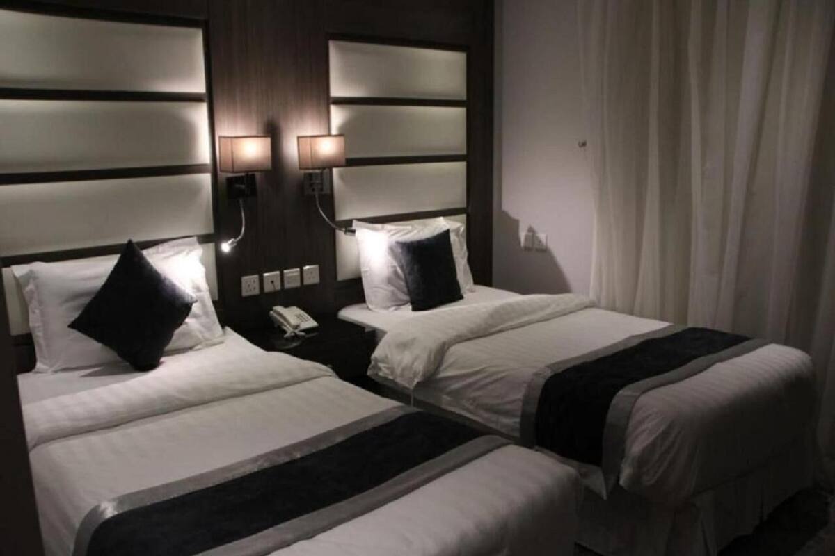 A hotel room with two beds, a nightstand with a phone, and a wall-mounted lamp.
