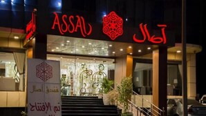 L’extérieur d’un hôtel, avec une enseigne bien visible portant l’inscription « ASSAL » et un logo décoratif au-dessus de l’entrée.