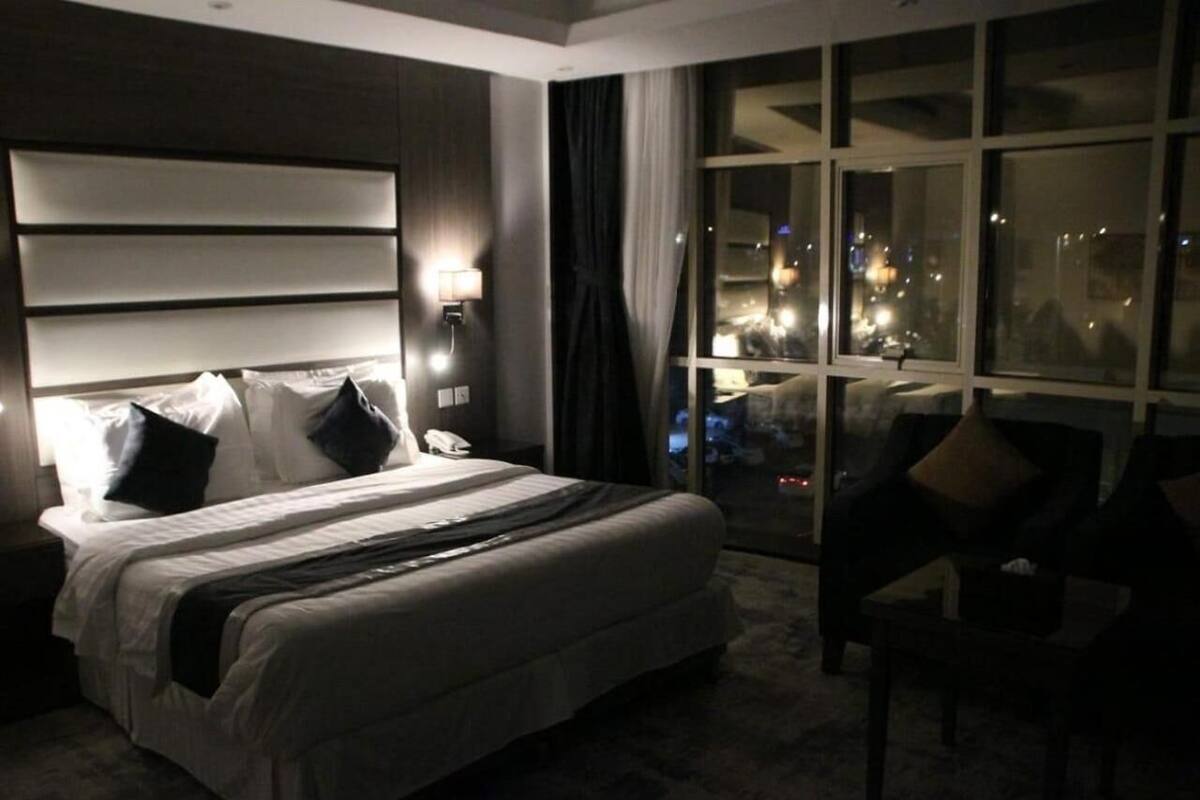 A hotel room with a large bed, a nightstand, a chair, and a view of the city at night.