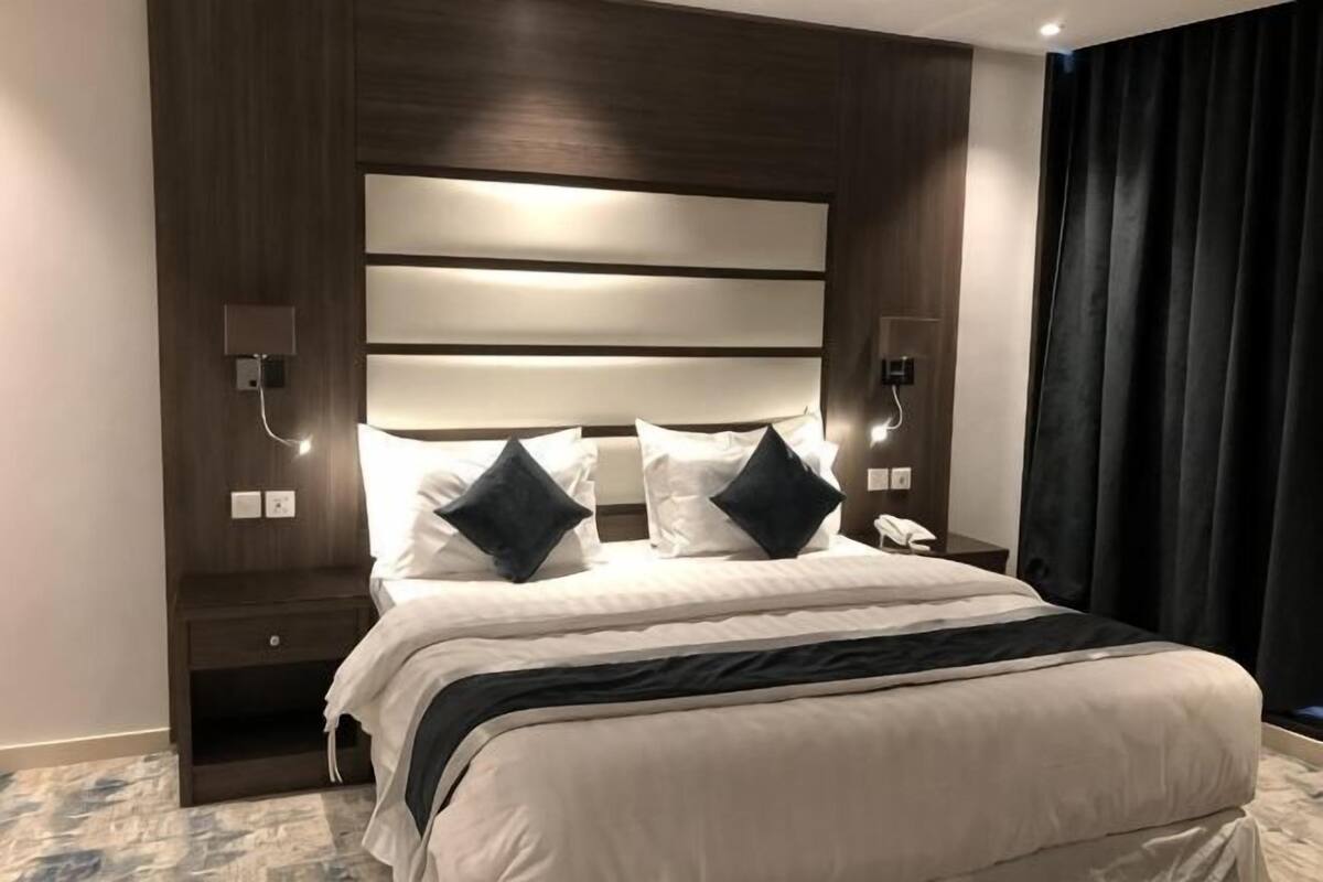 A hotel room with a large bed, bedside lamps, a nightstand, and a dark curtain.