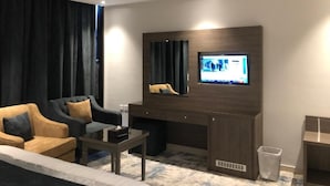 Une chambre d’hôtel moderne avec un mur d’accent en bois foncé, un téléviseur à écran plat fixé au-dessus d’un bureau en bois, un canapé et une table basse.