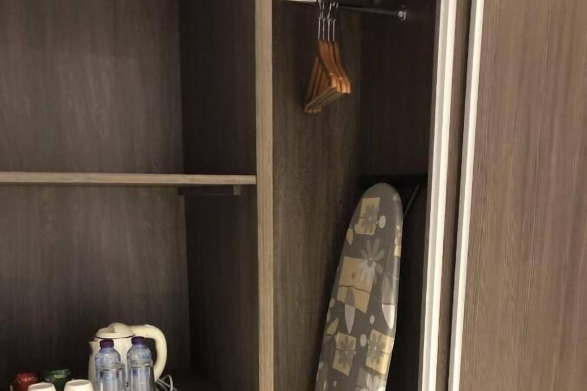 A wardrobe with a hanging iron, a tray with cups and bottles, and a shelf with a small item.