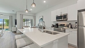 A modern kitchen with white cabinetry, stainless steel appliances, and a large island with bar stools.