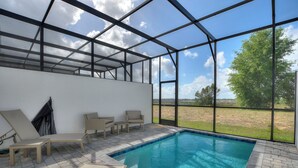 A swimming pool with lounge chairs and a view of the outdoors.