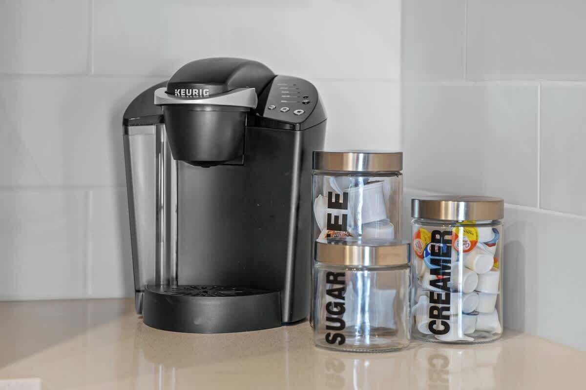 Une machine à café Keurig, un récipient à sucre et un pot à crème, posés sur un plan de travail.