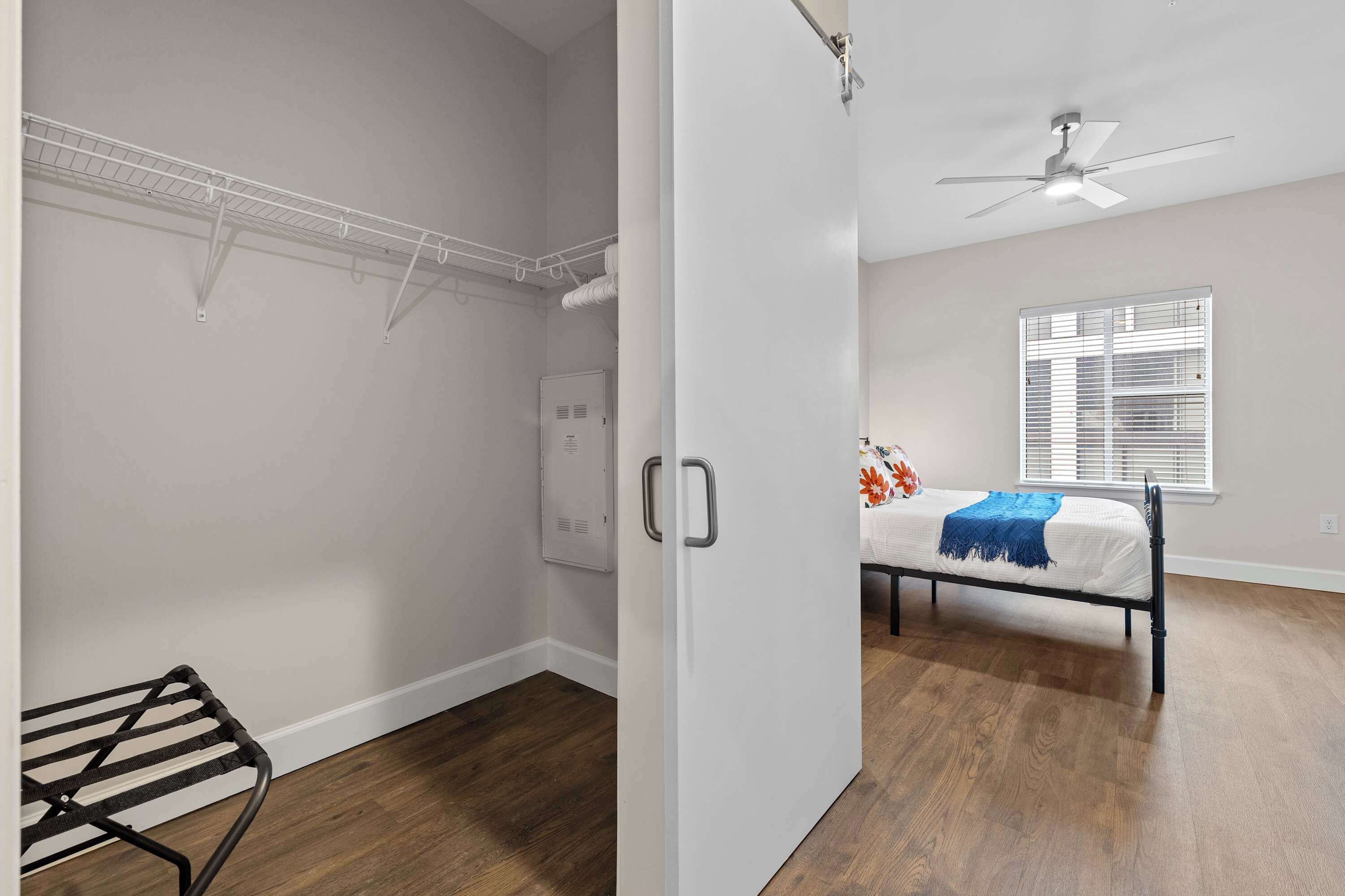 A bedroom with a bed, a ceiling fan, a window with blinds, and a white door.