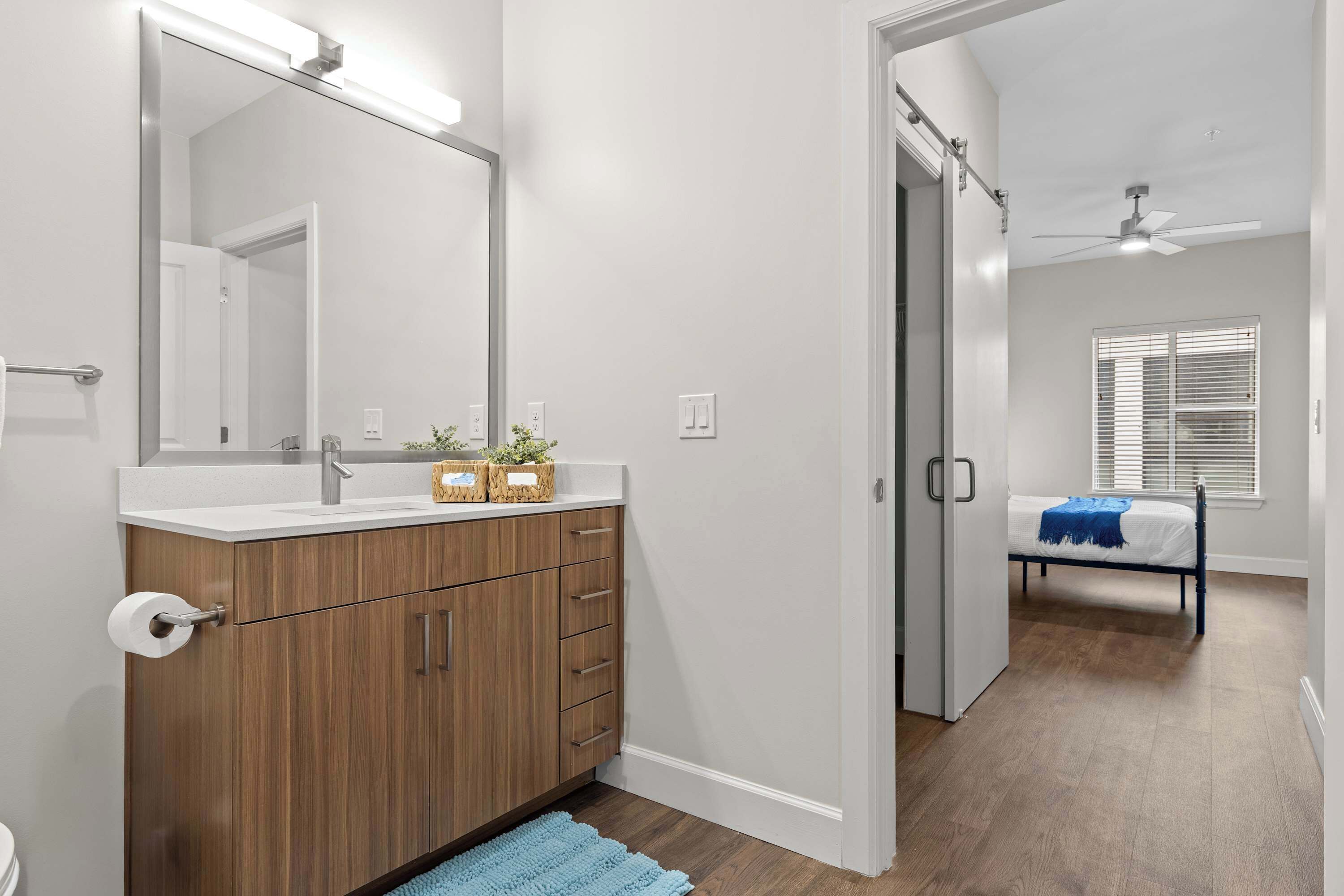 A bathroom with a wooden vanity, a large mirror, and a blue rug.