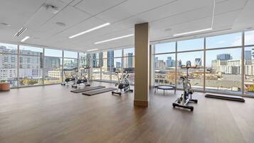 Une salle de sport spacieuse, dotée de grandes fenêtres, d’équipements d’exercice et offrant une vue sur la ville.