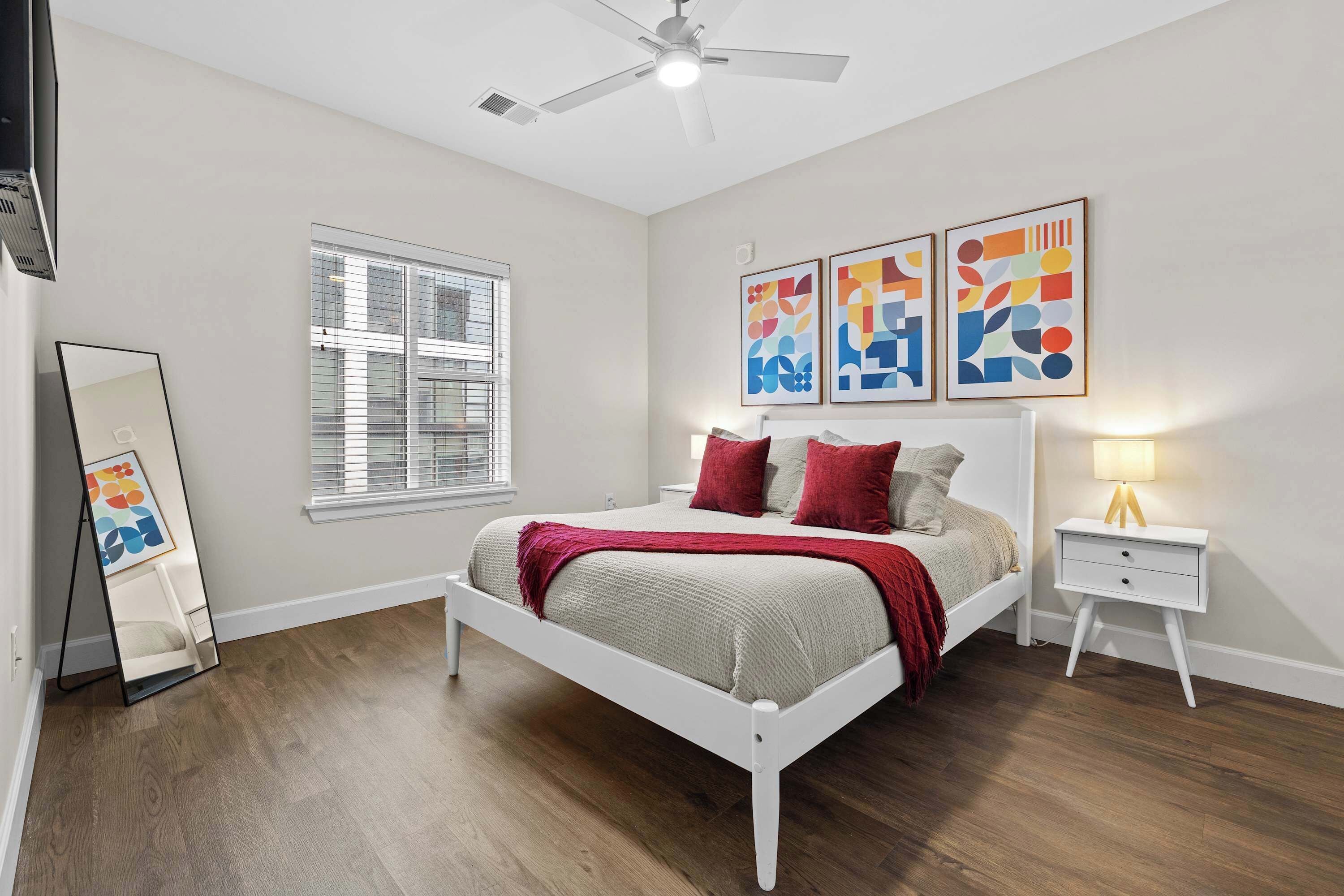 A bedroom with a bed, bedside tables, a ceiling fan, a window, and abstract wall art.