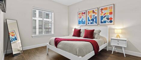 A bedroom with a bed, bedside tables, a ceiling fan, a window, and abstract wall art.