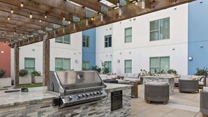 Un patio exterior con una estación de barbacoa de piedra, zona de estar y una pérgola con luces colgantes.