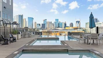 Une piscine sur le toit offrant une vue sur la ville, des chaises longues et un parasol bleu.