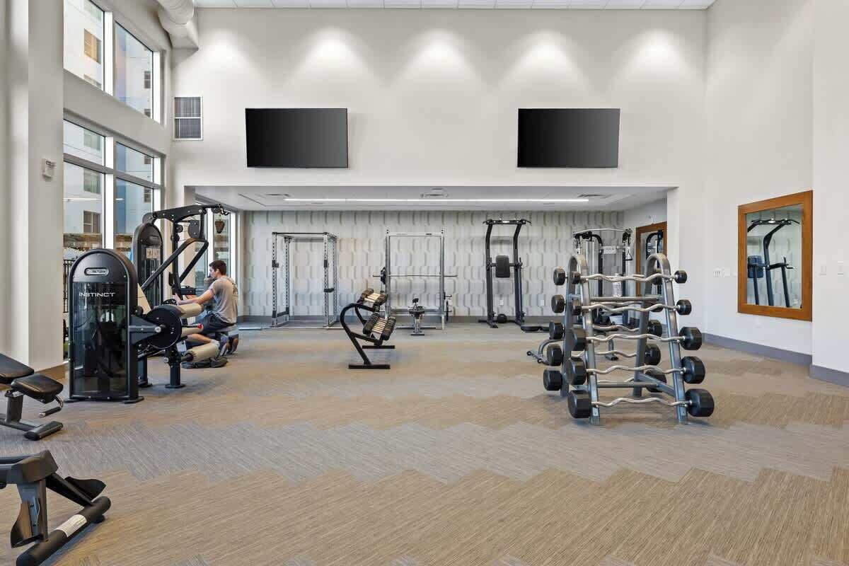 Ein geräumiger Fitnessraum mit unterschiedlichen Trainingsgeräten, großen Fenstern und einem aufgeräumten, modernen Design.