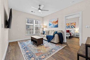 Un salon avec un ventilateur de plafond, un canapé, une table basse, un tapis et des œuvres d’art accrochées aux murs.