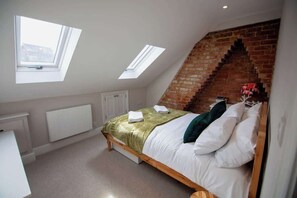 Un dormitorio con techo inclinado, tragaluces, pared de ladrillo, cama con almohadas y radiador.