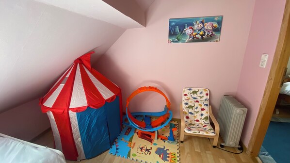 Una sala de juegos infantil con una tienda de campaña de temática circense, un gimnasio de juegos, una silla con estampado de dinosaurios y una pintura mural.