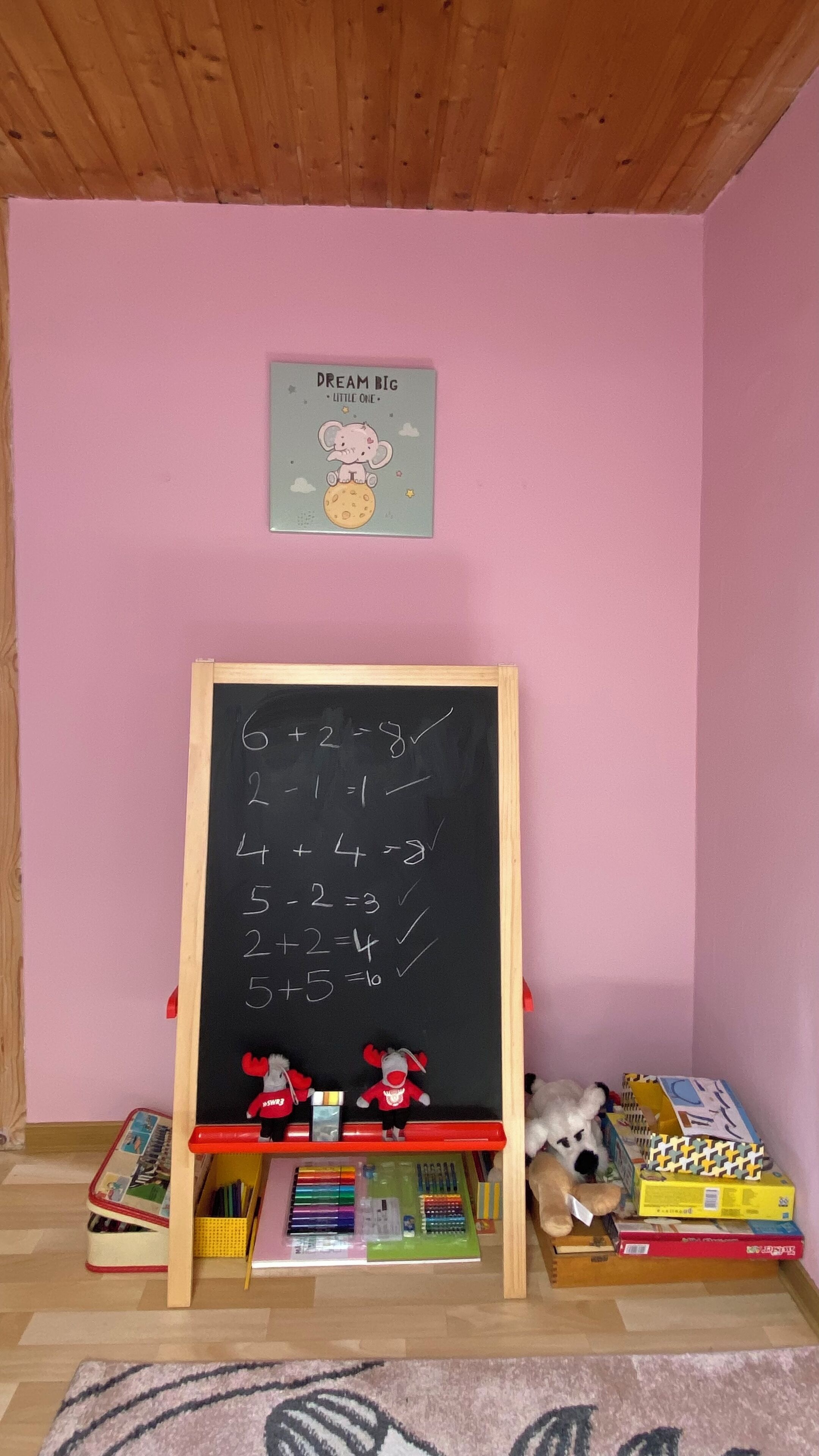 Un pequeño salón de clases con pared rosa, una pizarra con ecuaciones matemáticas y juguetes educativos.