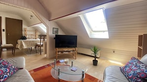 A cozy attic room with a dining area, a TV, and a glass coffee table. - Spacious vacation apartment in Falkenstein - in the middle of the Donnersbergkreis hiking region (Falkenstein)
