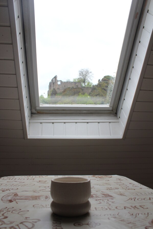 Ventana con tragaluz que muestra un edificio antiguo y una mesa con mantel blanco decorado con garabatos.
