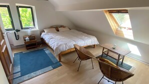 A bedroom with a bed, two windows, a table, and a chair. - Spacious vacation apartment in Falkenstein - in the middle of the Donnersbergkreis hiking region (Falkenstein)