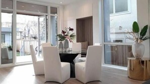 A modern dining area with a glass door leading to a balcony, white chairs, a table with a vase of flowers, and a large window with a view of the outside. - Point Grey Newly Constructed Estate (Vancouver)