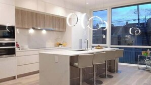 A modern kitchen with a central island, stainless steel appliances, and a large window providing a view of the outside. - Point Grey Newly Constructed Estate (Vancouver)