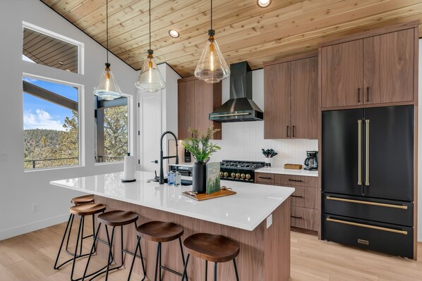 A modern kitchen with a large island, wooden cabinets, and a black refrigerator.